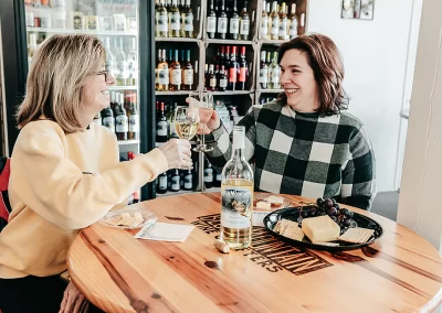 Two friends enjoying a bottle of win in front of a display of wines