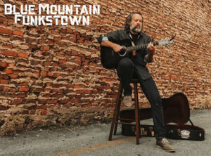 Paul McNeil Blue Mountain Paul McNeil with guitar against brick wall